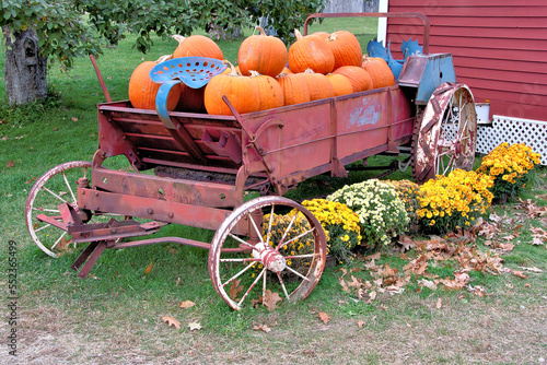 Colorful Autumn scene. Pumpkins stacked in antique manure spreader with rusty iron wheels located on farm near Greenville, New Hampshire. photo