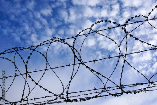 razor wire fence against blue sky with fluffy white clouds. security barbed wire fence. restriction barrier.
