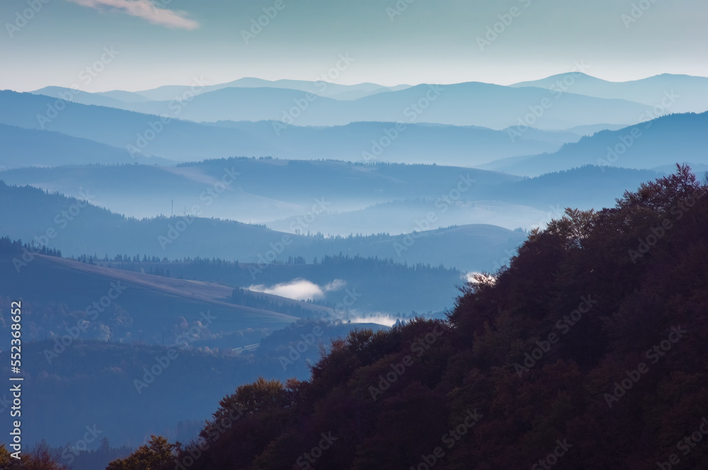 Morning autumn mountain landscape. Behind the forested hill lie mountain ranges in a blue mist