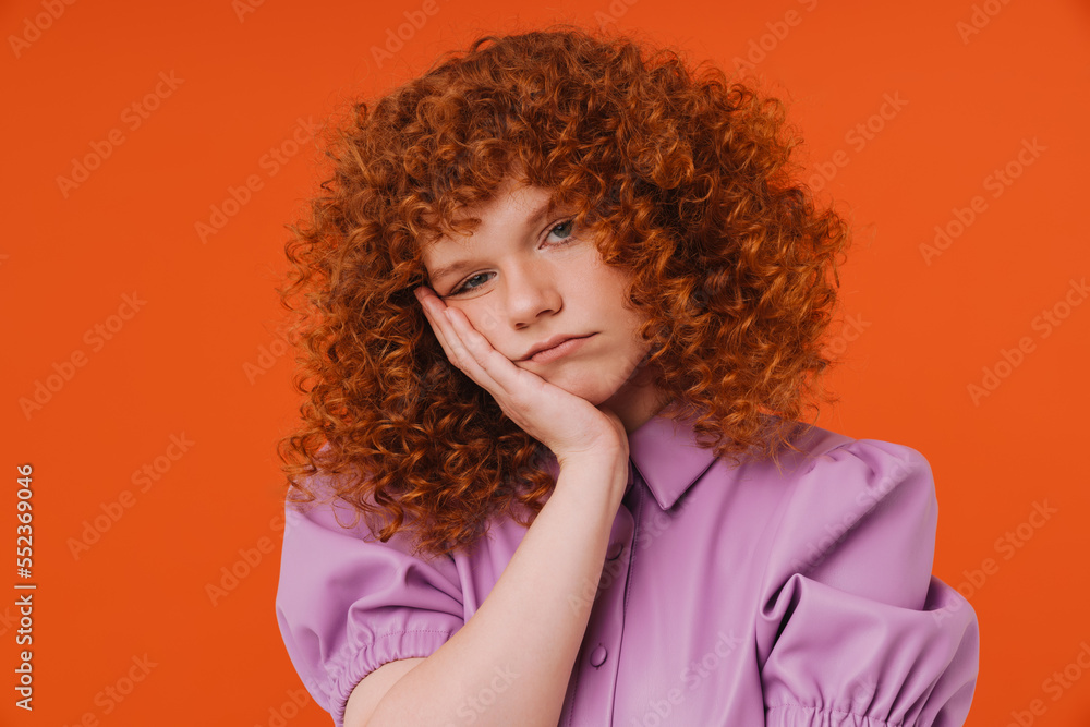 Bored redhead girl putting her cheek on palm isolated over orange background Bored redhead girl putting her cheek on palm isolated over orange background