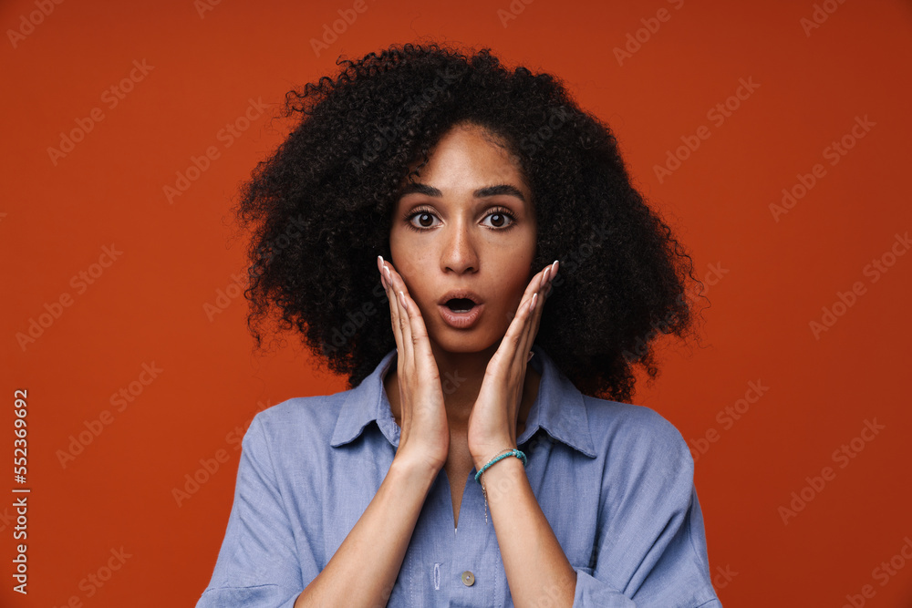 Surprised african woman standing with opened mouth isolated over red wall Surprised african woman standing with opened mouth isolated over red wall