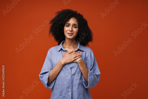 Sad african american woman holding hands on chest and looking at camera isolated