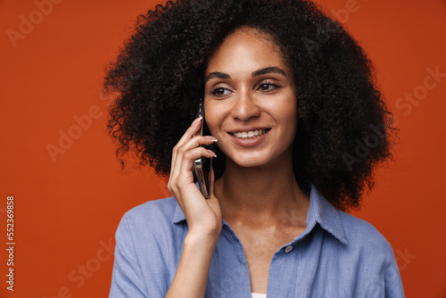Smiling african american woman talking on mobile phone isolated over red wall