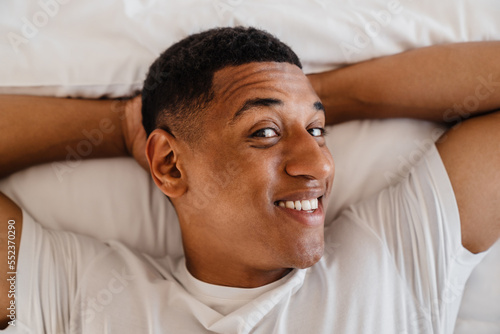 Top view of joyful african man lying with his hands under head in bed at home