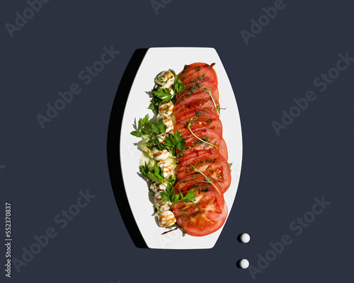 Caprese salad with mozzarella, tomato and balsamic sauce in white plate top view isolated on blue background