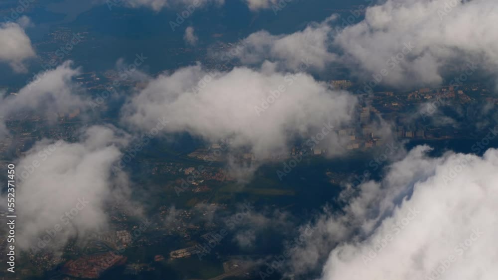 Top view of the city and fluffy white clouds. First-person view from the porthole. To fly by plane. Cinematic shot in flight from the window Top view of the city and fluffy white clouds. First-person view from the porthole. To fly by plane. Cinematic shot in flight from the window