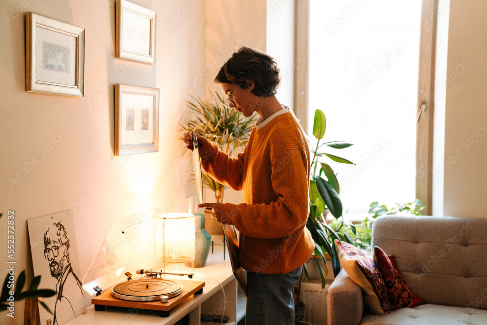 Brunette young woman holding vinyl record while using stereo turntable Brunette young woman holding vinyl record while using stereo turntable