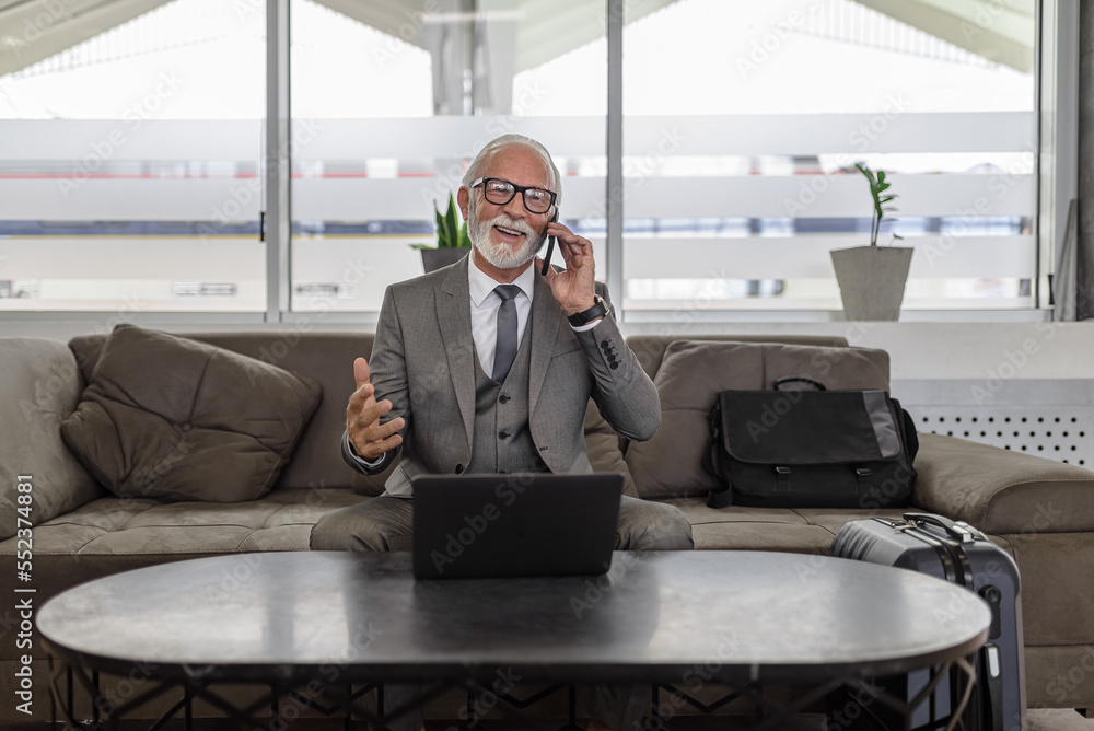 Happy entrepreneur or businessman talking on smart phone while using laptop in hotel hall Happy entrepreneur or businessman talking on smart phone while using laptop in hotel hall