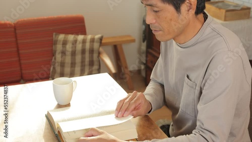 Middle aged asian man reading English book at home. 25P.