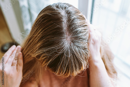 Close-up top view of woman's head with flowing blond hair, gray growing roots that require coloring photo