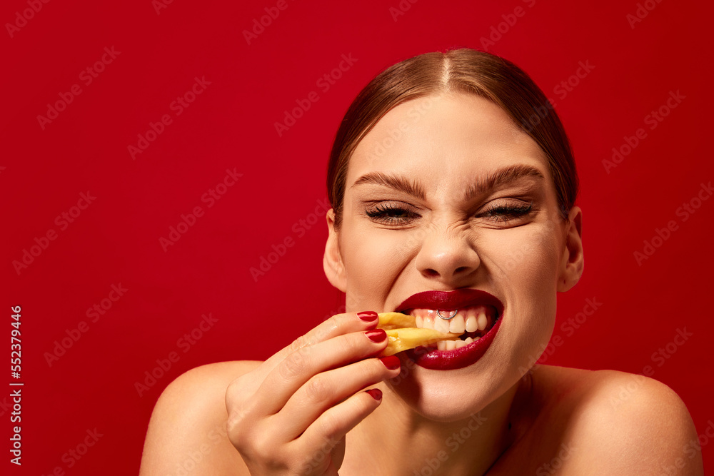 Emotive young woman eating fried potato, fries over vivid red background. Junk food lover. Delicious taste. Food pop art photography. Emotive young woman eating fried potato, fries over vivid red background. Junk food lover. Delicious taste. Food pop art photography.