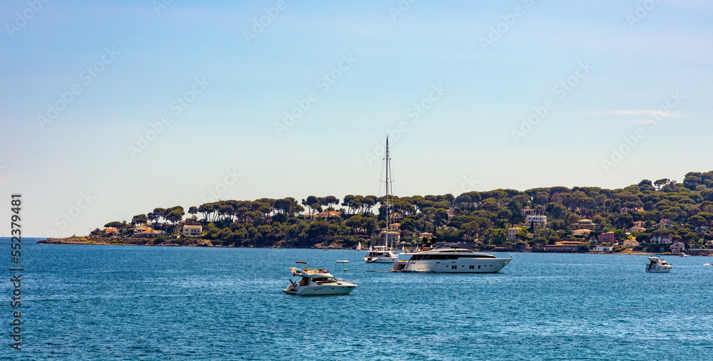 Fototapeta premium Panoramic view of harbor and exclusive residential peninsula along Plage del la Salis beach onshore Azure Cost of Mediterranean Sea in Antibes resort town in France
