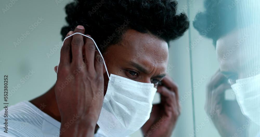 Blck african man removing covid mask looking out pensive