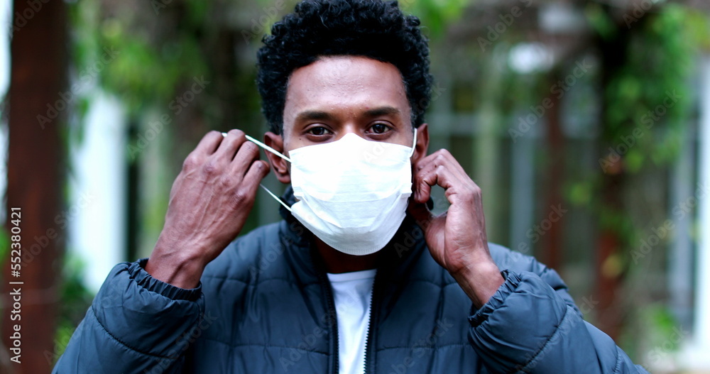 Black man removing covid virus mask outdoors looking to camera Black man removing covid virus mask outdoors looking to camera