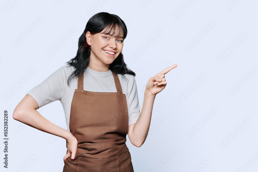 Young woman in an apron pointing with fingers to the side, empty space for advertising Young woman in an apron pointing with fingers to the side, empty space for advertising