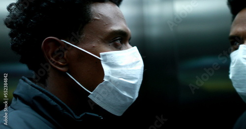African american man putting on covid mask inside elevator, black person portrait pandemic