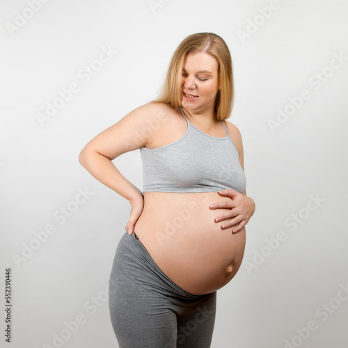 Free Download A pregnant girl, on a gray background. Big stomach, back pain. - GFXLoad