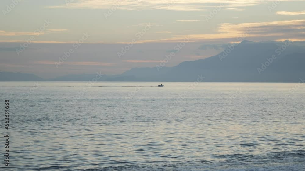 A small fishing boat in the open sea sails toward the mountains and into the sunset. Beautiful soft evening light. High quality 4k footage A small fishing boat in the open sea sails toward the mountains and into the sunset. Beautiful soft evening light. High quality 4k footage