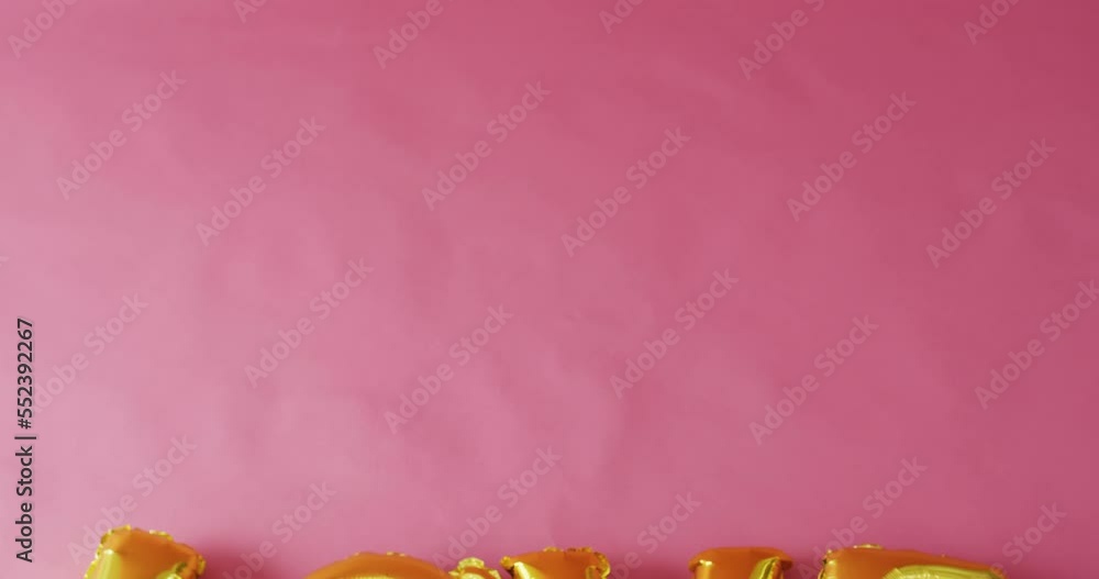 Overhead video of shiny gold love text balloon, on pink background with copy space Overhead video of shiny gold love text balloon, on pink background with copy space