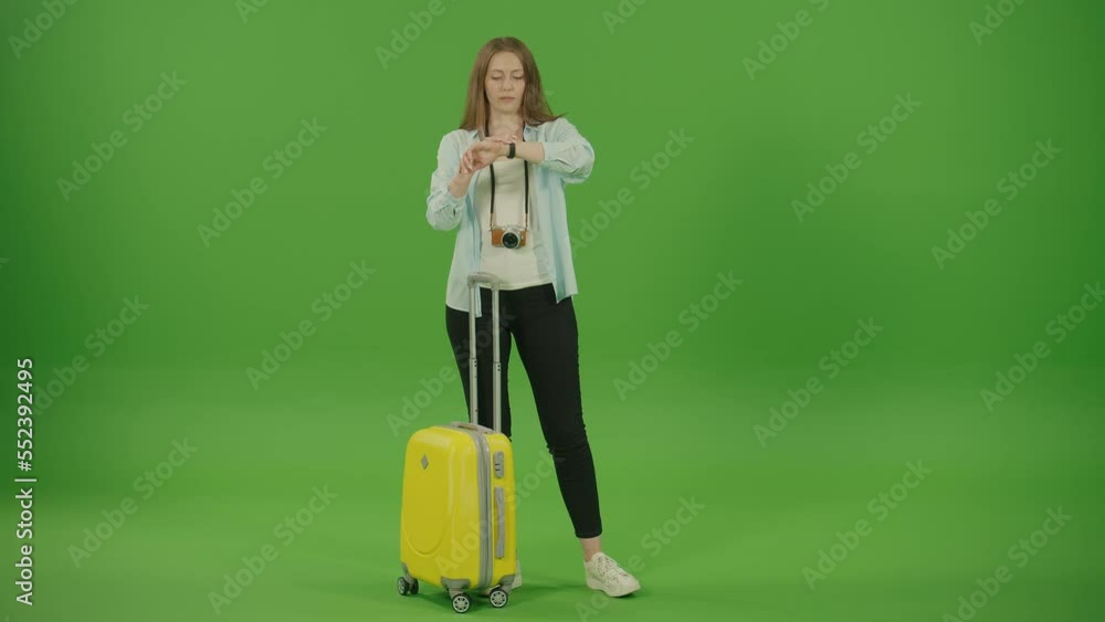 Green Screen. Chroma Key. Pretty Woman Tourist With Yellow Luggage in the Hands is Checking Time While Waiting Something. Women are Nervous While Waiting and Taking Photo on the Camera Green Screen. Chroma Key. Pretty Woman Tourist With Yellow Luggage in the Hands is Checking Time While Waiting Something. Women are Nervous While Waiting and Taking Photo on the Camera
