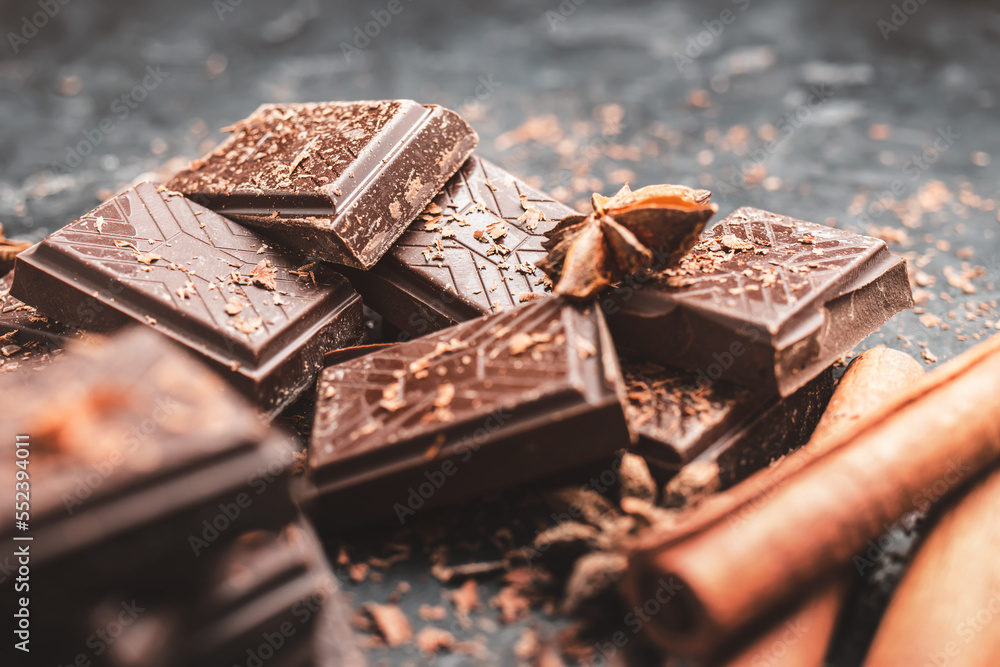 Dark chocolate bar pieces on dark background with grated chocolate and spices, pile chunks of broken chocolate Dark chocolate bar pieces on dark background with grated chocolate and spices, pile chunks of broken chocolate