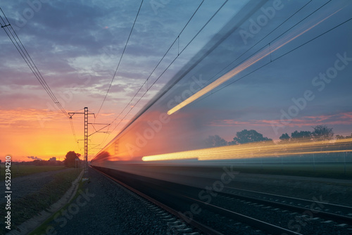 Modern railway at beautiful sunrise. Light trail of train on railroad track. Moving modern intercity passenger train..