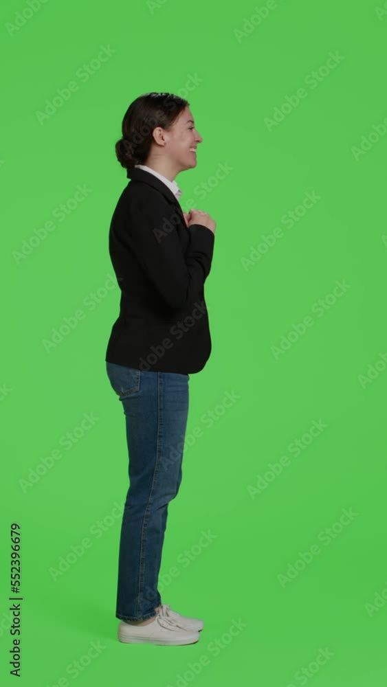 Vertical video: Profile of cheerful office worker waving hello or goodbye on camera, doing greeting gesture over green screen backdrop. Young happy businesswoman saying hi in studio, wearing suit on Vertical video: Profile of cheerful office worker waving hello or goodbye on camera, doing greeting gesture over green screen backdrop. Young happy businesswoman saying hi in studio, wearing suit on