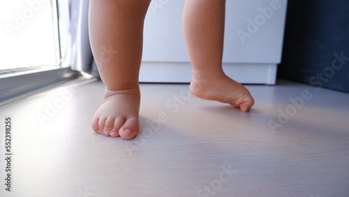 Toddler doing first steps on wooden floor at home, baby's feet walking © Татьяна Буйницкая