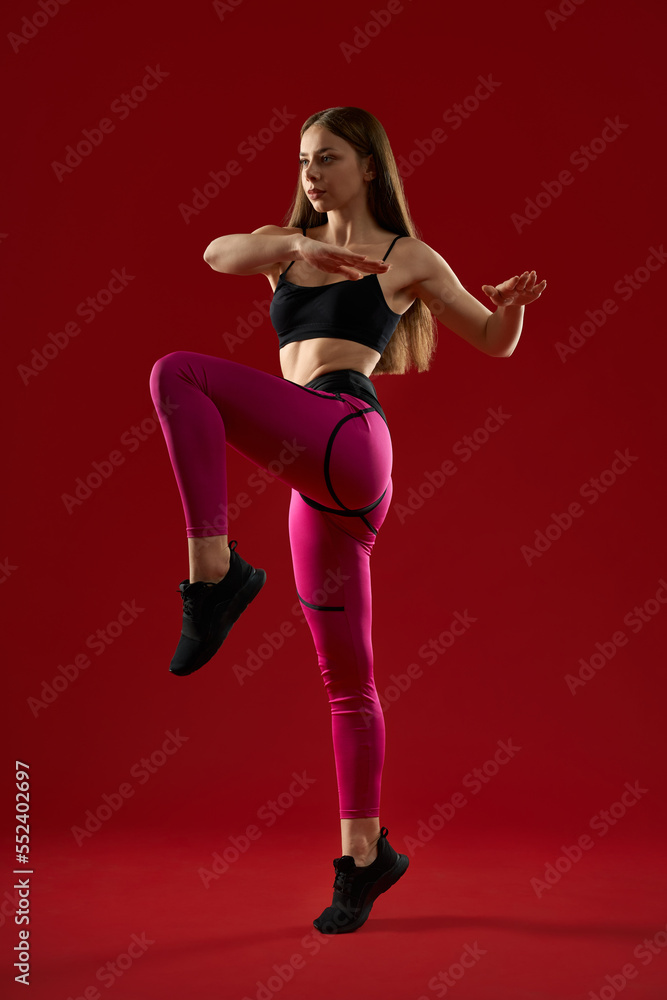 Pretty brunette athletic woman with long hair jumping keep balance by hands, on red studio background. Pretty strong female training in air. Concept of martial arts.