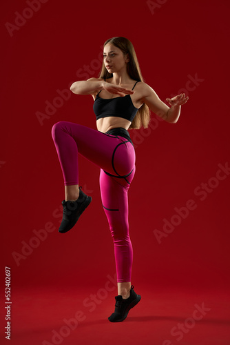 Pretty brunette athletic woman with long hair jumping keep balance by hands, on red studio background. Pretty strong female training in air. Concept of martial arts. © serhiibobyk