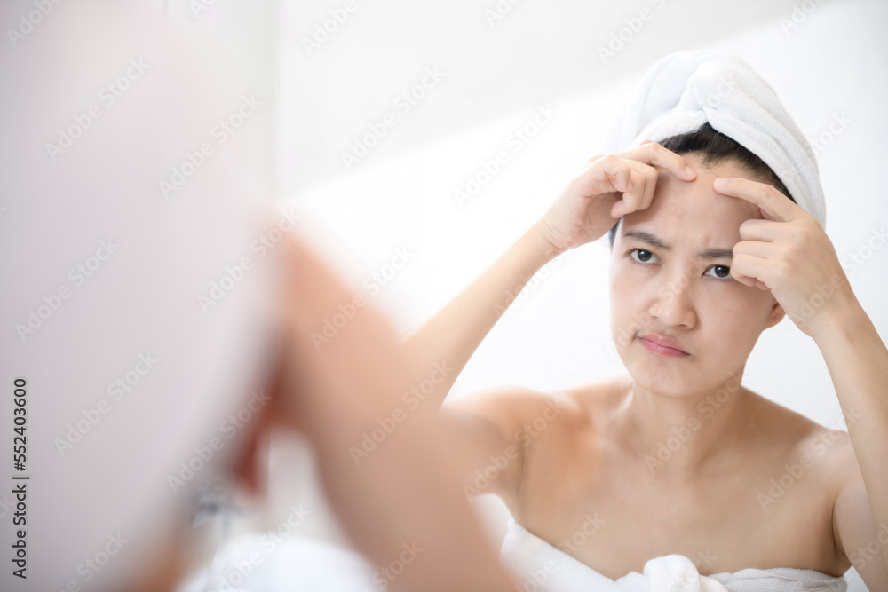 Problem skin. Concerned young asian women popping pimple on cheek while standing near mirror in bathroom. young asian women with acne Problem skin. Concerned young asian women popping pimple on cheek while standing near mirror in bathroom. young asian women with acne