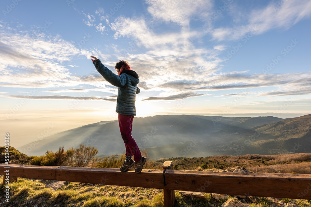 girl balancing on the mountain with the sun in the background and sun rays through the clouds girl balancing on the mountain with the sun in the background and sun rays through the clouds