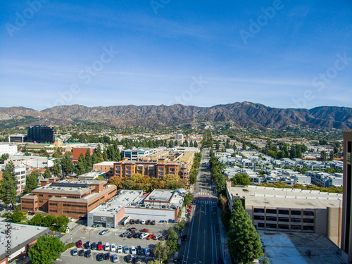aerial shot of office buildings, apartments and shops surrounded by lush green trees, cars driving and parked on the street with majestic mountains and a clear blue sky in Burbank California USA photo