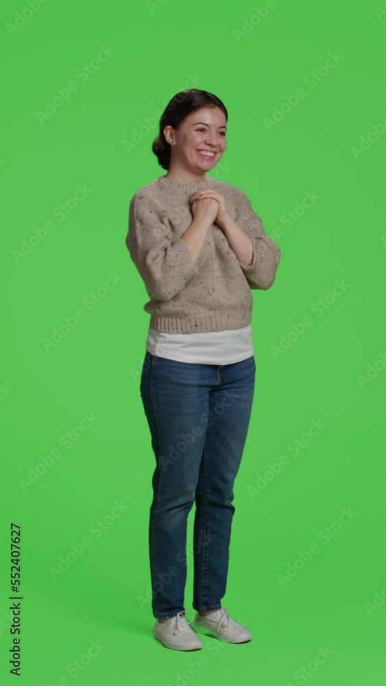 Vertical video: Side view of model greeting people with wave, smiling on camera. Relaxed woman waving hi or hello in studio, standing over full body green screen background and saying goodbye or greet Vertical video: Side view of model greeting people with wave, smiling on camera. Relaxed woman waving hi or hello in studio, standing over full body green screen background and saying goodbye or greet