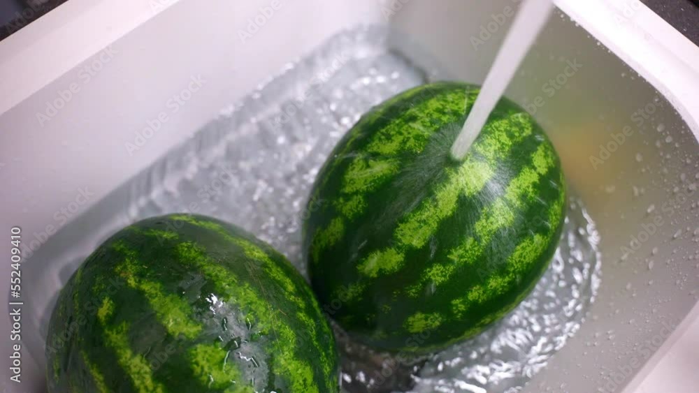 Two striped round watermelons in white sink under the water flow, top