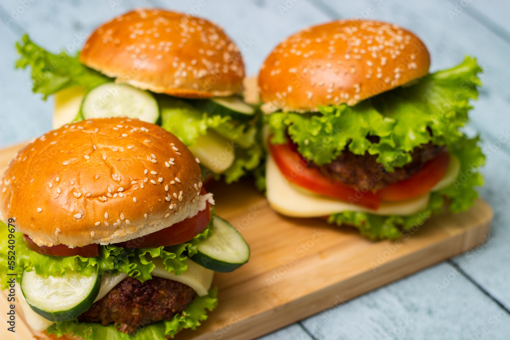 Burgers with beef meat, cheese and lettuce, served on cutting board Burgers with beef meat, cheese and lettuce, served on cutting board