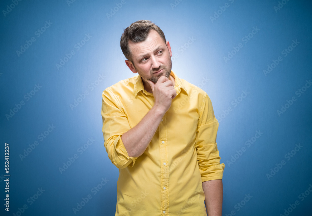 Annoyed guy looking to side over blue background, dresses in yellow shirt Annoyed guy looking to side over blue background, dresses in yellow shirt