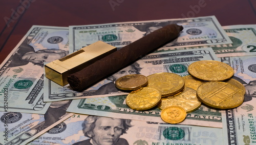 Golden coins on a background of 20 dollar bills with a Cuban cigar and vintage golden lighter