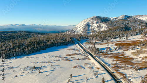 Aerial view of a narrow road through snow covered mountains on a sunny morning with a clear blue sky and copy space