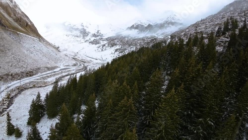 FPV Aerial view of car driving down on a frozen mountain road covered with snow. High altitude road. Highway on the mountain. Frozen mountain road in winter season. Winding road closed. Mountain fores photo