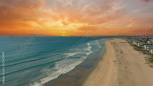 aerial shot of the coastline with blue ocean water and homes along the sand on the beach, cars driving on the street and powerful clouds at sunset in Huntington Beach California USA