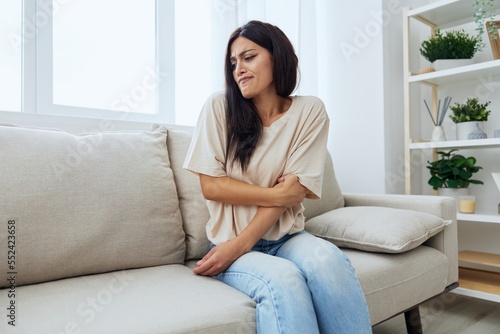 Woman sitting on sofa at home arm and shoulder pain, muscle sprain and joint pain, calcium problems in bones