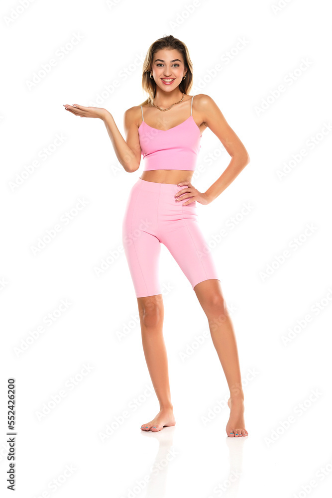 Smiling Woman In Pink Leggings And Top Presenting Something On her Empty Palm On A White Background Smiling Woman In Pink Leggings And Top Presenting Something On her Empty Palm On A White Background