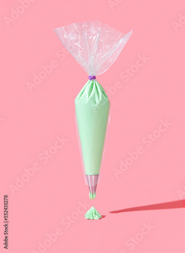 Frosting bag isolated on a pink background. Green buttercream icing in a plastic bag