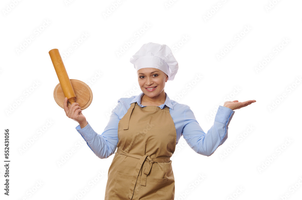 Cheerful pretty woman cook, baker confectioner in chef's hat and beige apron holding rolling pin and wooden board in one hand and imaginary copy space on the other, isolated over white background Cheerful pretty woman cook, baker confectioner in chef's hat and beige apron holding rolling pin and wooden board in one hand and imaginary copy space on the other, isolated over white background