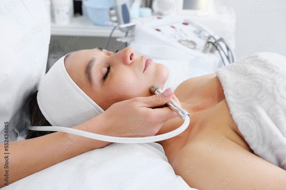 The cosmetologist makes the procedure Microdermabrasion of the skin of the face of a beautiful, young woman in a beauty salon. Cosmetology and professional skin care. The cosmetologist makes the procedure Microdermabrasion of the skin of the face of a beautiful, young woman in a beauty salon. Cosmetology and professional skin care.