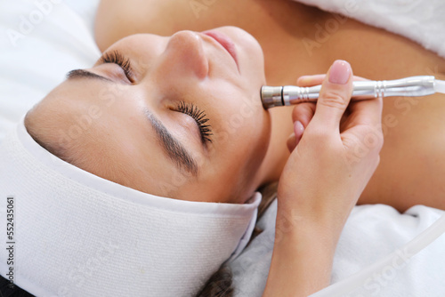 The cosmetologist makes the procedure Microdermabrasion of the skin of the face of a beautiful, young woman in a beauty salon. Cosmetology and professional skin care. photo