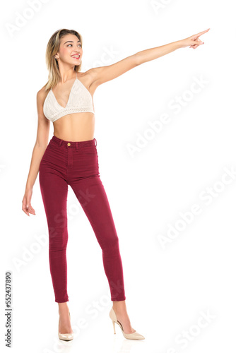 Smiling Woman In Burgundy Jeans And Top Presenting Something ,Touching, Showing Direction On A White Background