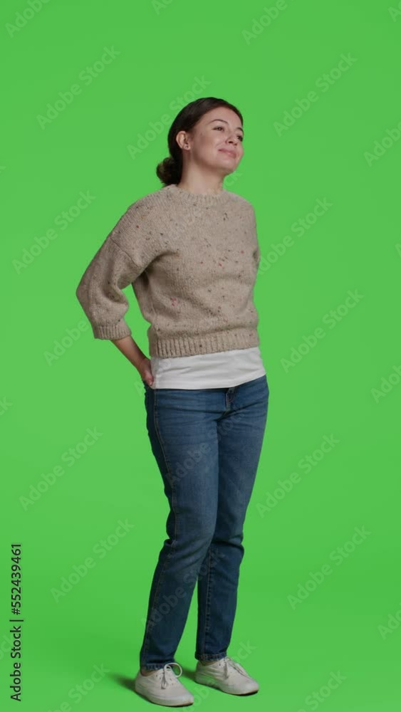 Vertical video: Side view of caucasian girl posing on full body green screen background, looking at camera and being happy. Young adult acting confident in studio, standing over isolated greenscreen Vertical video: Side view of caucasian girl posing on full body green screen background, looking at camera and being happy. Young adult acting confident in studio, standing over isolated greenscreen