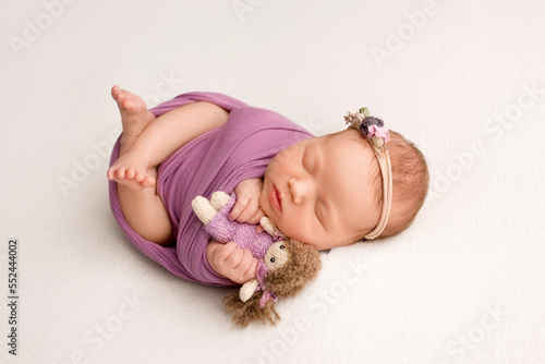 Sleeping newborn girl in the first days of life on a white background. A newborn baby in a purple lilac winding and a headband. Hand, palms of father and mother, parents hold the child.